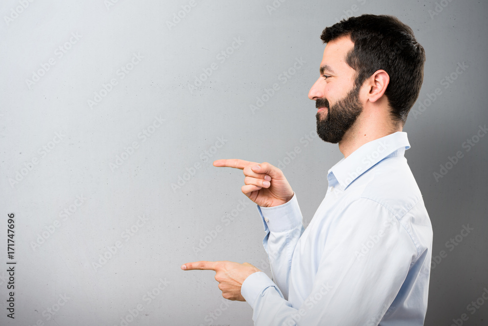 Handsome man with beard pointing to the lateral on textured background Handsome man with beard pointing to the lateral on textured background
