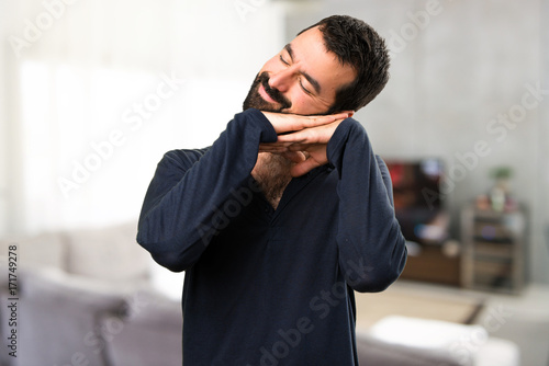 Handsome man with beard making sleep gesture inside house