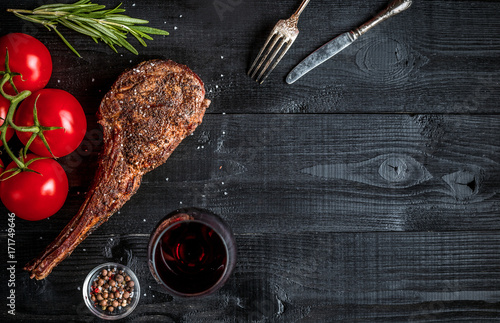 Barbecue dry aged rib of beef with spice, vegetables and glass of red wine close-up on black wooden background photo