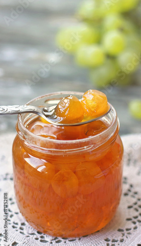 Slatko - preserved white grapes on silver spoon, in glass jar, on wooden background; traditional serbian desert of white grapes or white cherries photo