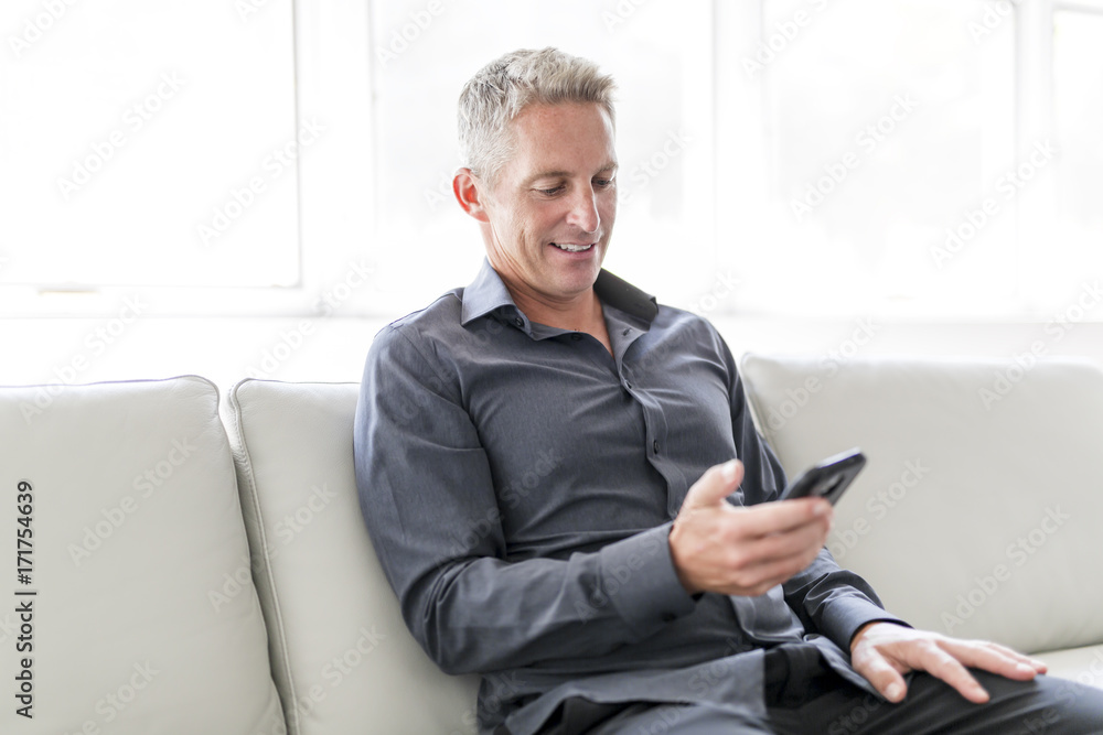 Portrait of mature man relaxing at home in sofa and cellphone