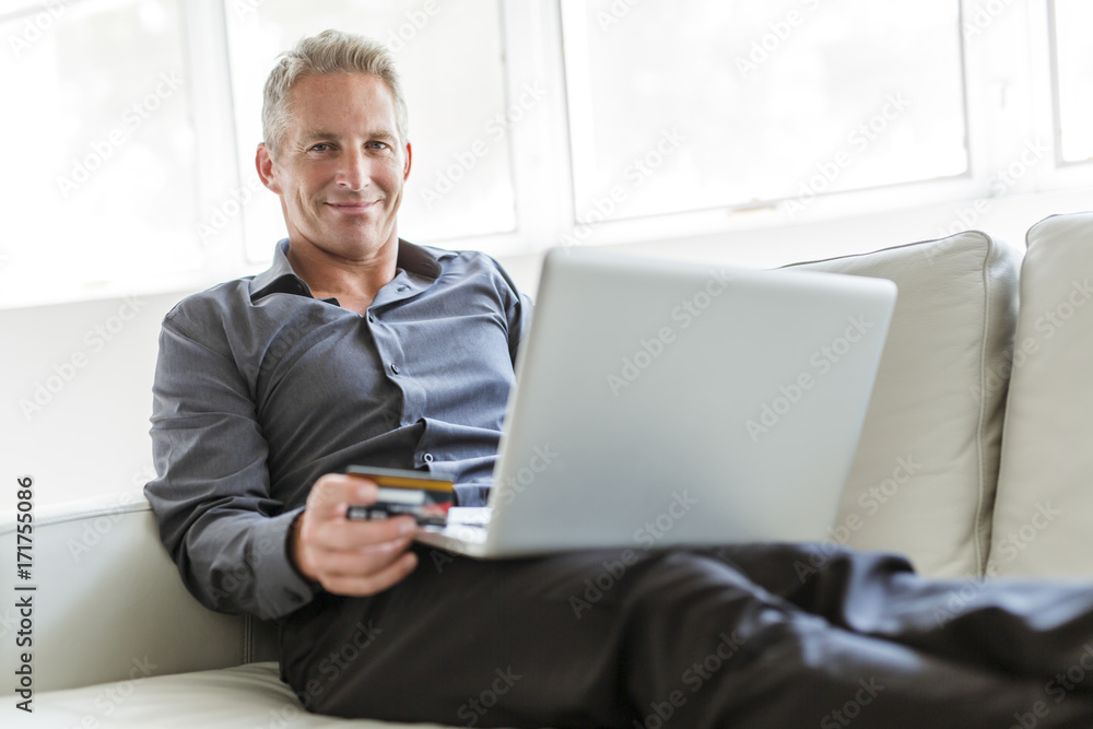 Portrait of happy mature man using laptop lying on sofa in house Portrait of happy mature man using laptop lying on sofa in house