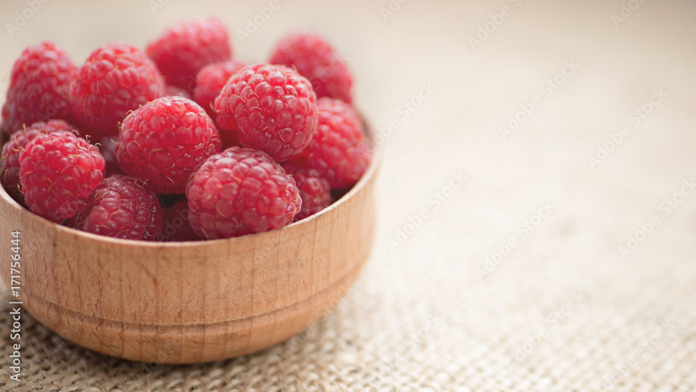 Organic raspberry in wooden bowl on burlap background Organic raspberry in wooden bowl on burlap background