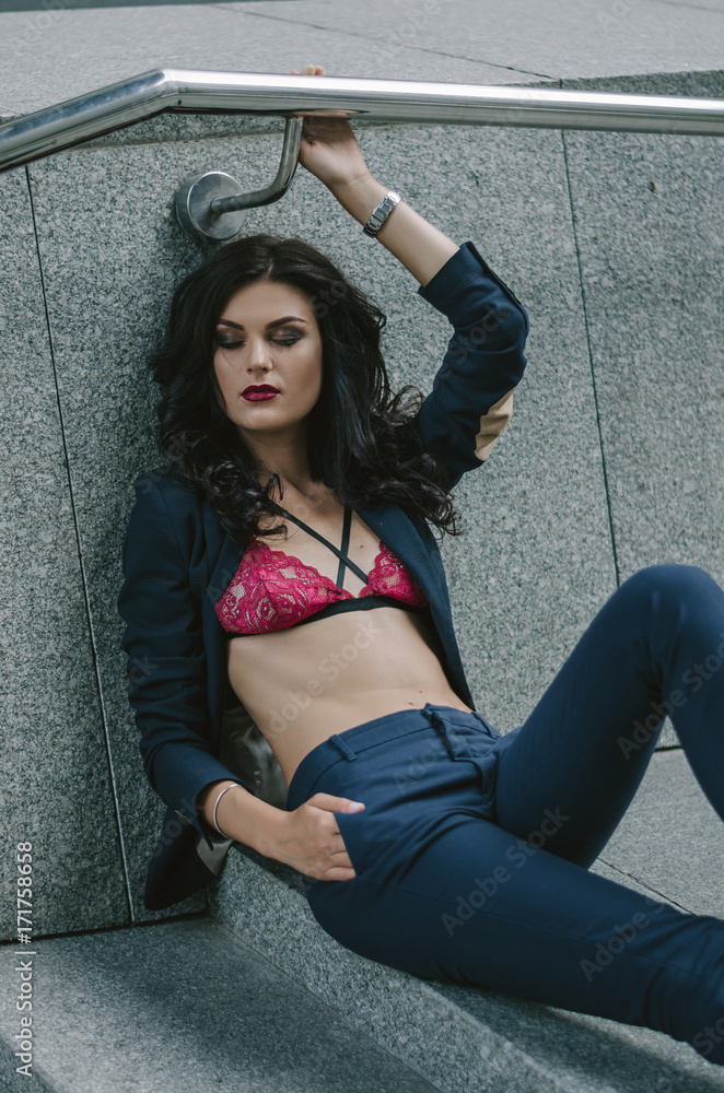 a stylish fashionable sexy brunette in a blue suit and a red bra is lying  on the steps in the city. Fashion photo Stock Photo