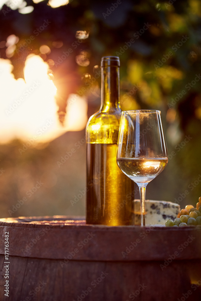 Obraz premium Glass of white wine and bottle with food at sunset
