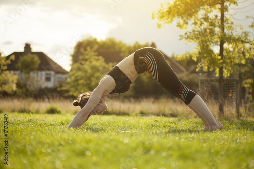 Young brunette doing yoga and stretching back park during sunset
