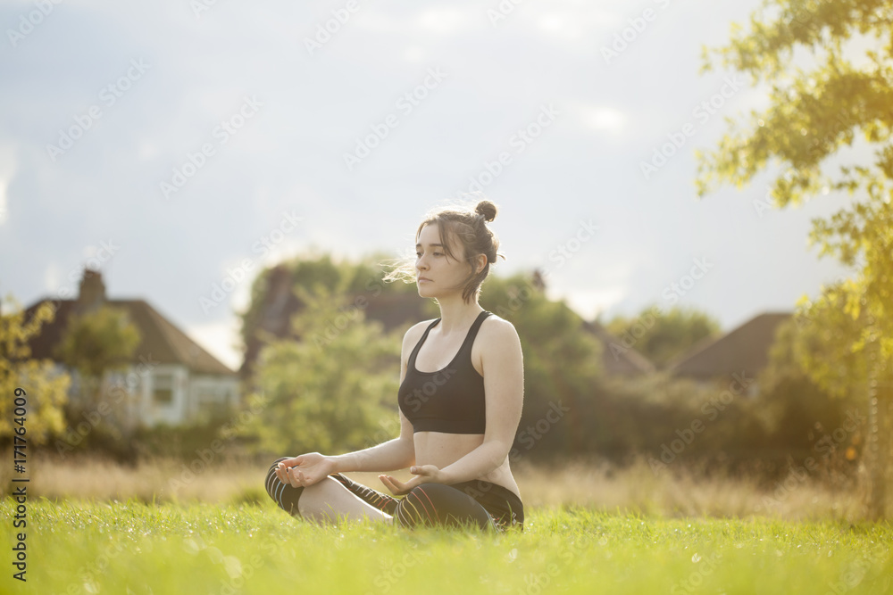 Fototapeta premium Young woman doing yoga and meditating in park
