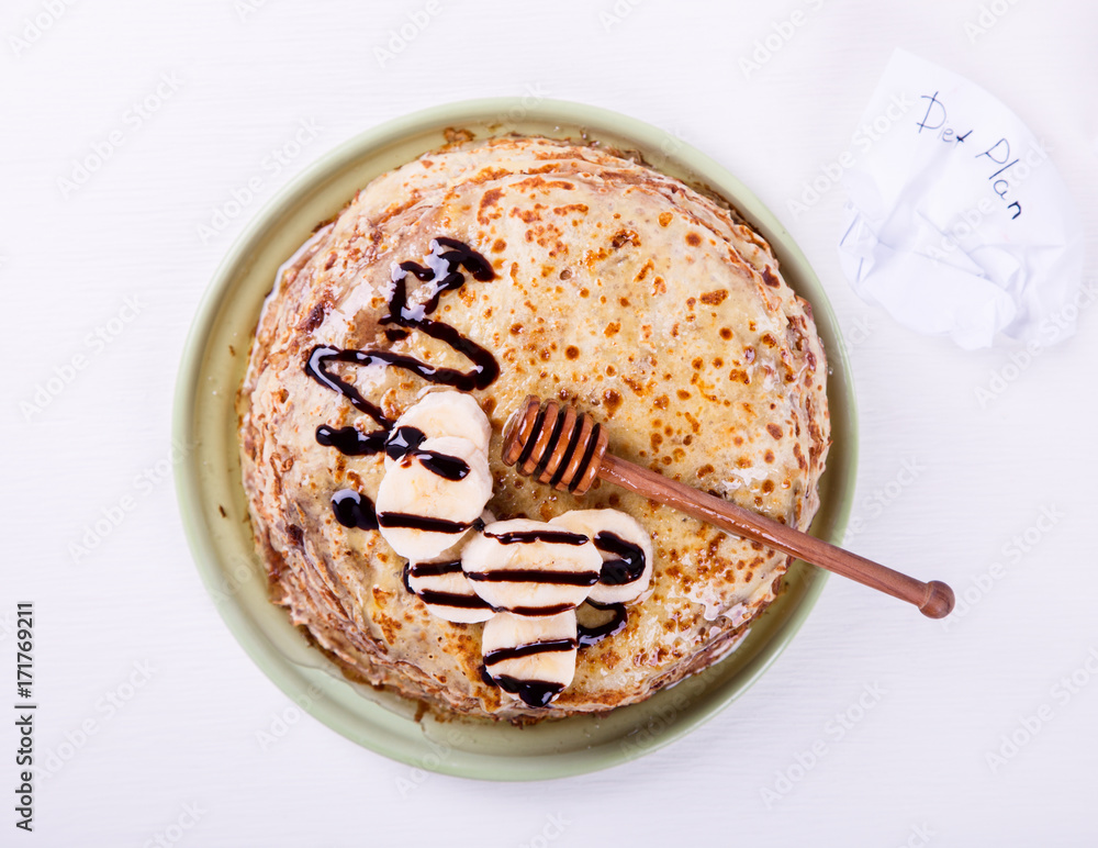 Fototapeta premium Stack of Thin pancakes with Honey,Banana,Chocolate. on a White Background.Tradition,Holiday,Dessert,Breakfast,Pastries.Copy space for Text. selective focus.