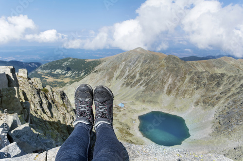 Legs of traveler sitting on a high mountain top with lake view.
