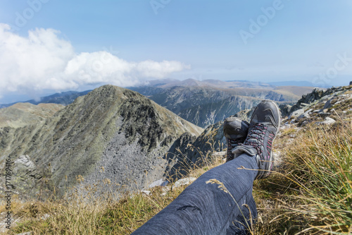 Legs of traveler sitting on a high mountain top with rocky peaks.Musala peak in Bulgaria