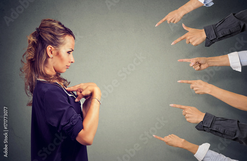 Blaming you. Anxious angry woman judged by different people pointing fingers hands at her. photo