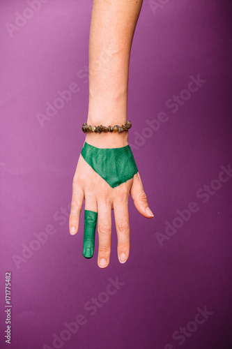 one woman hand, Caucasian painted green hand skin, purple magenta background, jewelery bracelet