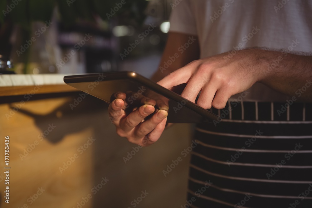 Mid section of waiter using tablet by counter