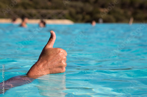 Man's hand is pushed out of the water and shows a thumbs-up