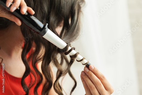 Hairstylist curling hair client in hairdressing salon