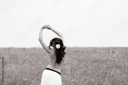 Portrait in vintage tones and texture woman in a lacy skirt and a bare back is standing in the field and enjoying herself and nature. The concept of self-love and harmony with the environment