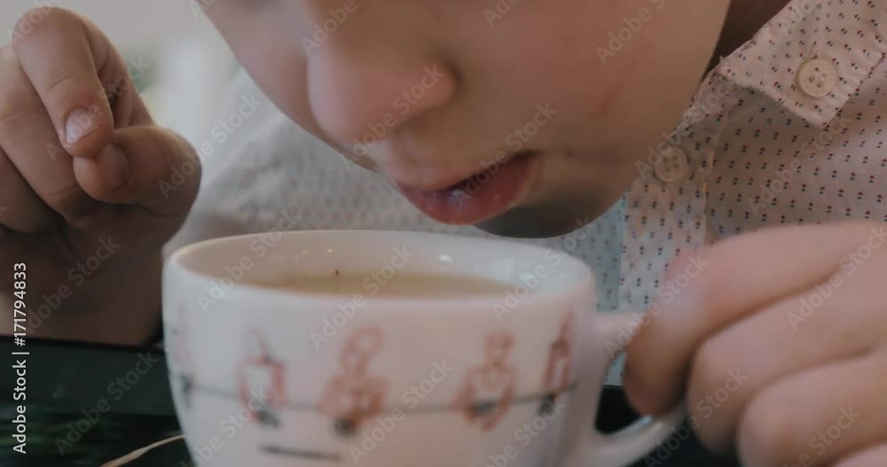 Close-up shot of a child blowing on the cup of hot tea with milk trying to cool it Close-up shot of a child blowing on the cup of hot tea with milk trying to cool it