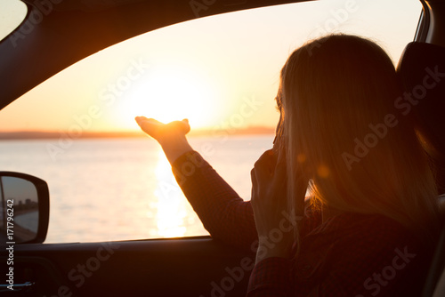 Young woman looking out car window of the sunset on the sea and talking on the phone. © Denis