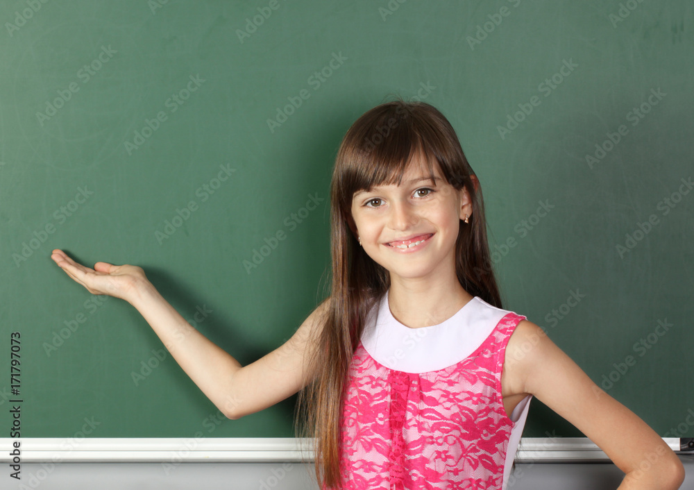 Smiling child girl holds his hand near empty school blackboard, copy space Smiling child girl holds his hand near empty school blackboard, copy space