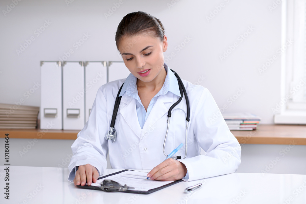 Doctor woman filling up medical form while sitting at the desk. Medicine and health care concept Doctor woman filling up medical form while sitting at the desk. Medicine and health care concept