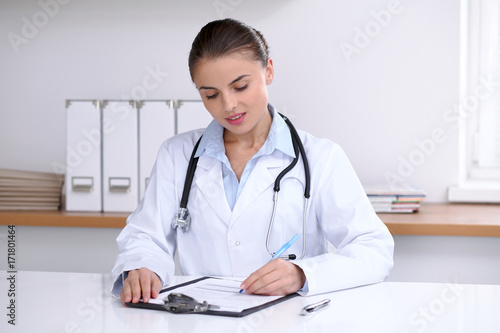 Doctor woman filling up medical form while sitting at the desk. Medicine and health care concept