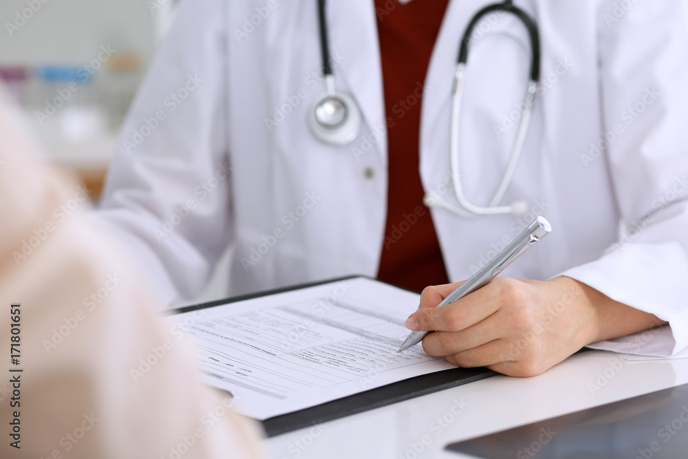 Close up of a female doctor filling up an application form while consulting patient Close up of a female doctor filling up an application form while consulting patient