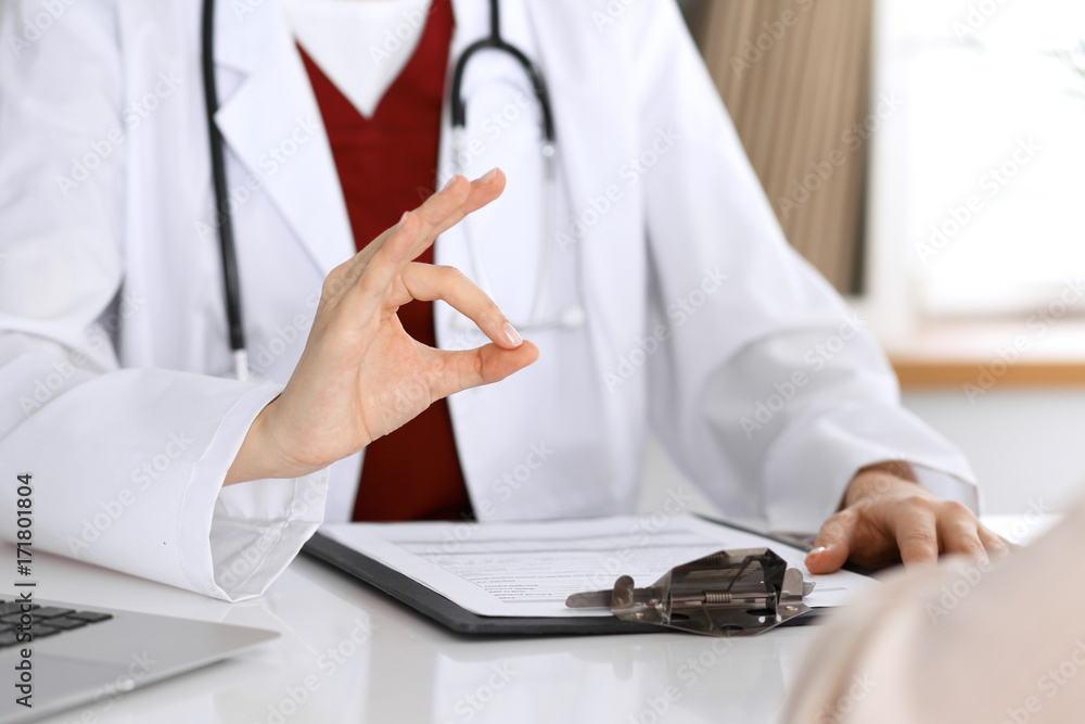 Close up of a doctor hand showing ok sign while phusician and his patient discussing medical records after health examination Close up of a doctor hand showing ok sign while phusician and his patient discussing medical records after health examination