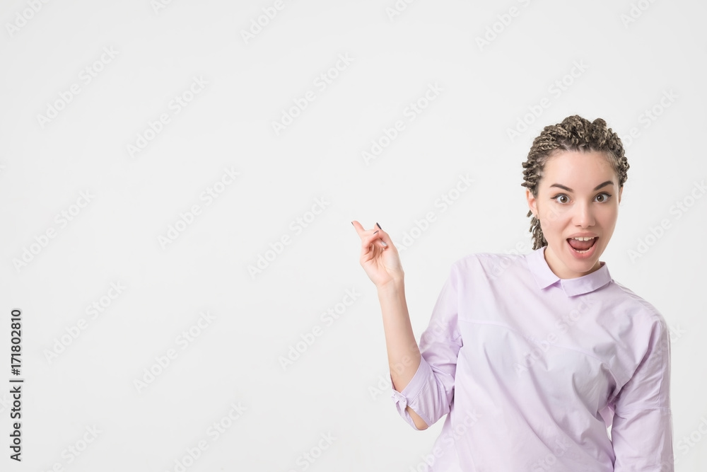Shocked caucasian woman with braids hairstyle and good mood showing with index finger aside.