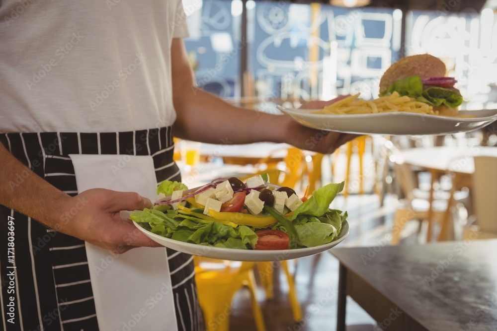 Mid section of waiter serving salad and French fries