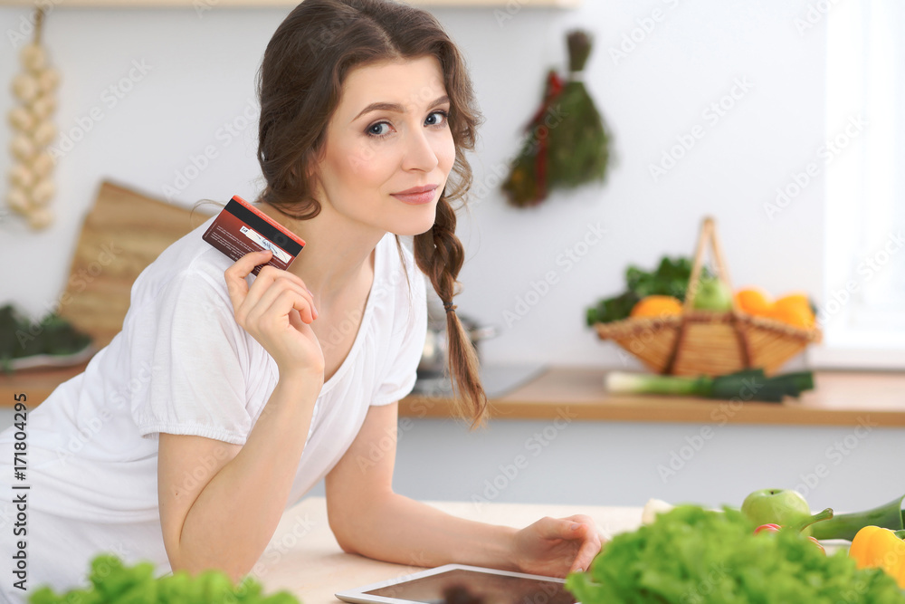 Young  woman looking for a new recipe for  cooking in a kitchen. Housewife is making online shopping by tablet computer and credit card