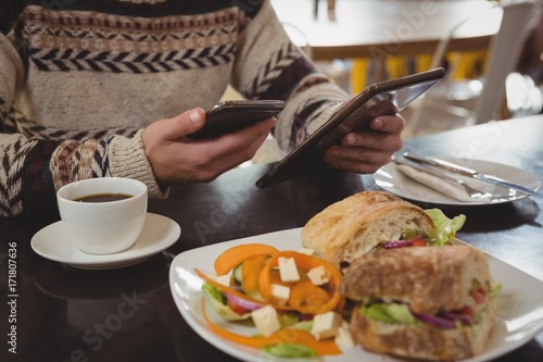 Mid section of man with breakfast using phone and tablet in cafe