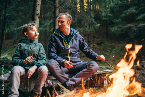 Father and son roast marshmallow candies on the campfire in forest