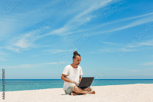 young man with laptop on the beach