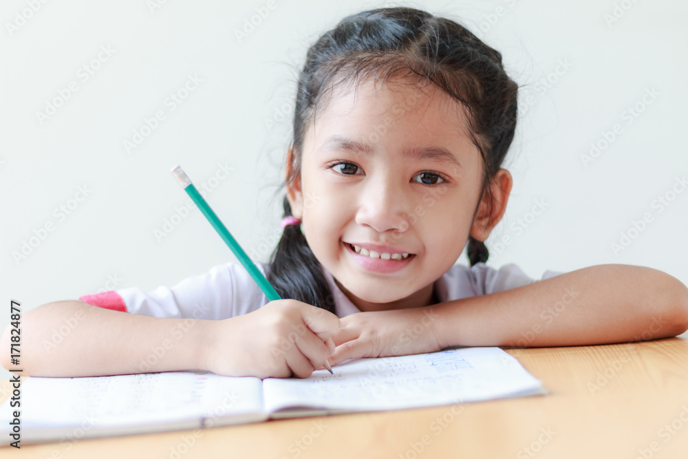 Portrait of Asian little girl in Thai kindergarten student uniform doing homework and smiling with happiness Portrait of Asian little girl in Thai kindergarten student uniform doing homework and smiling with happiness