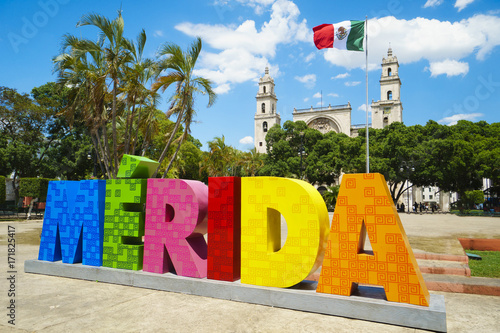 MERIDA, MEXICO - MAY 23, 2017: Colorful sign Merida with mexican flag and cathedral on a street in sunny summer day photo