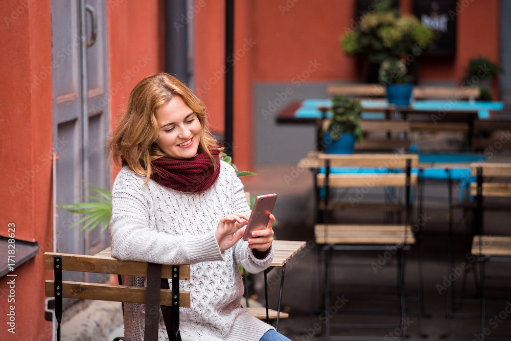 Woman is sitting in an street cafe and looking at phone. Woman is sitting in an street cafe and looking at phone.