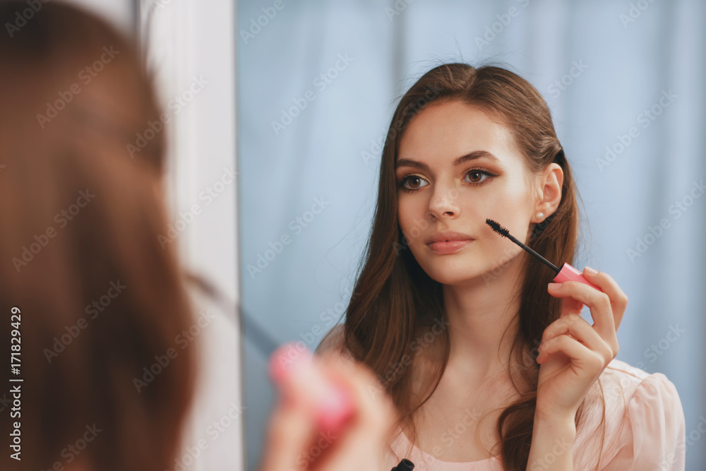Young beautiful girl makes herself a makeup in front of a mirror