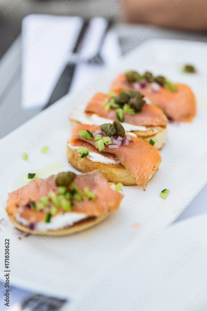 Smoked Salmon on Grilled Seven Grain Bread topping with prickled and sliced cucumber on the white plate at restaurant in Dubai. Smoked Salmon on Grilled Seven Grain Bread topping with prickled and sliced cucumber on the white plate at restaurant in Dubai.