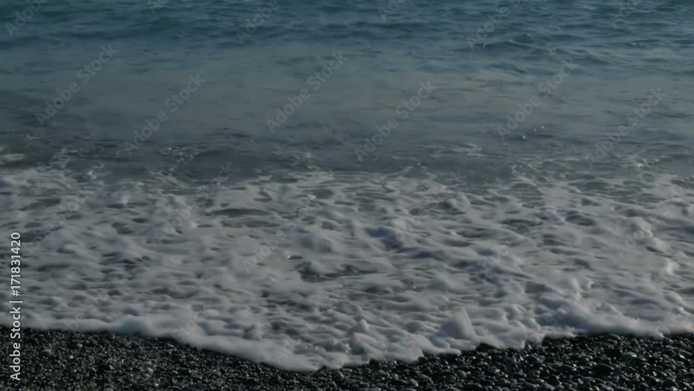 Large transparent waves with foam. Sea pebble beach with colorful stones Large transparent waves with foam. Sea pebble beach with colorful stones
