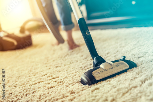 Woman using a vacuum cleaner while cleaning carpet in the house.