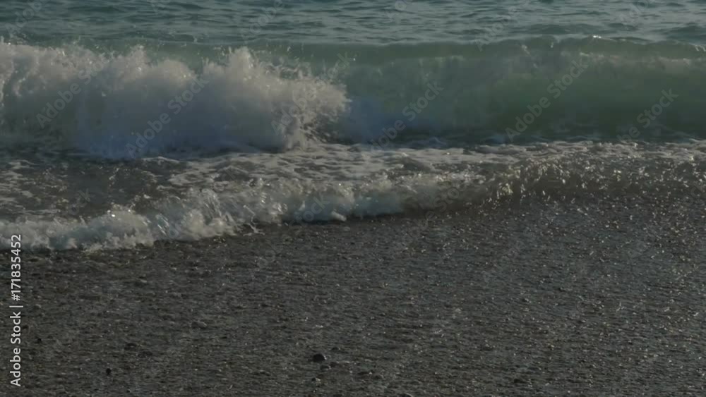 Large transparent waves with foam. Sea pebble beach with colorful stones Large transparent waves with foam. Sea pebble beach with colorful stones