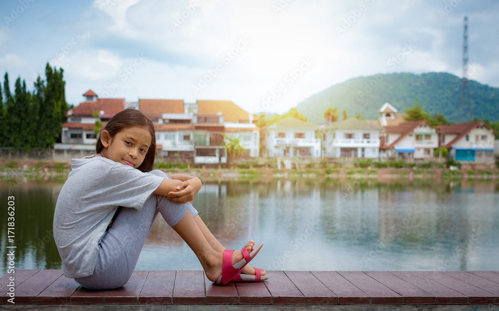 Lovely girl sitting near natural pond with housing estate.