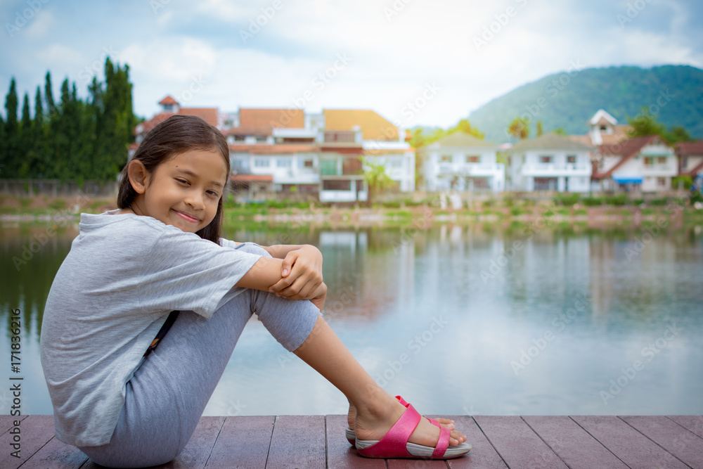 Lovely girl sitting near natural pond with housing estate.