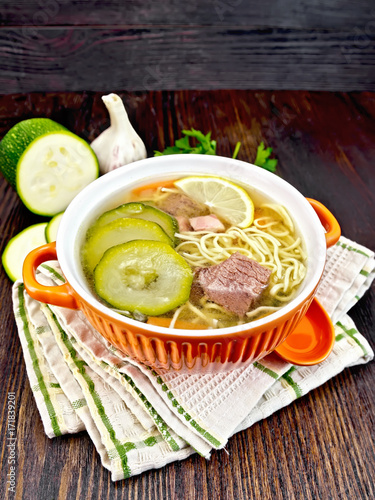Soup with zucchini and noodles in red bowl on towel