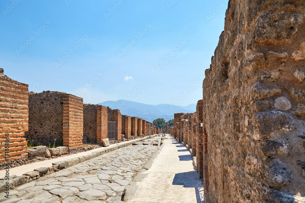 A street without people with the ruins of houses in Pompeii with Vesuvius in the background