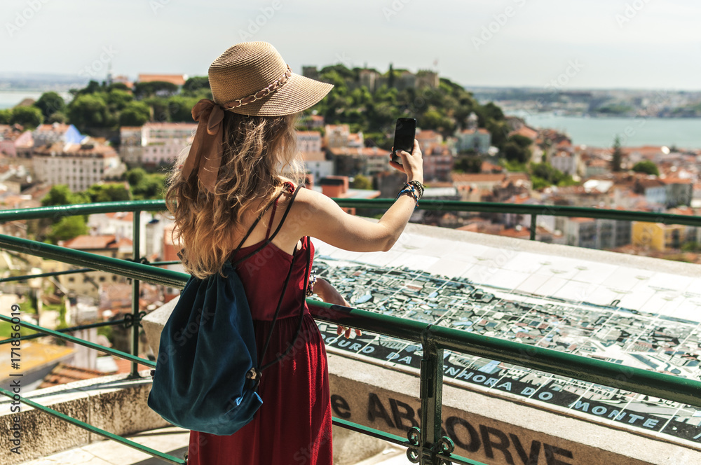 Woman is using a smartphone and looking at a panoramic view on the city of Lisbon in Portugal