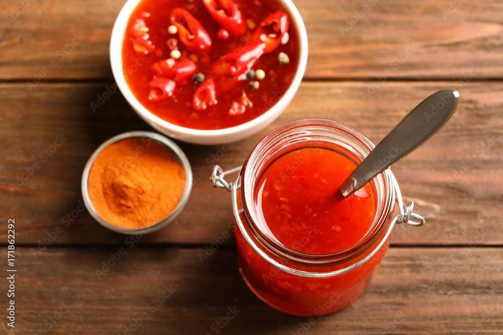 Delicious chili sauce in kitchenware on wooden table Delicious chili sauce in kitchenware on wooden table