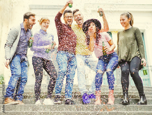 Canvas Print Group of happy friends having a street party drinking beers while confetti are f
