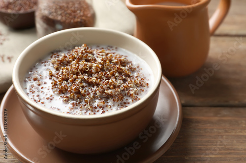 Bowl with boiled quinoa grains and milk on wooden table