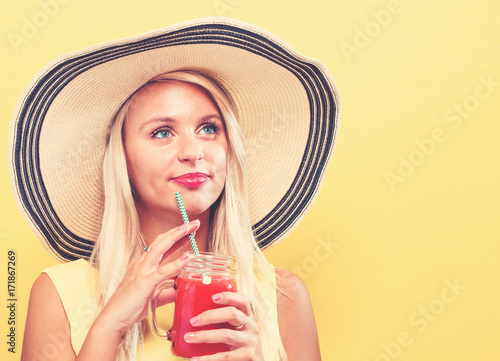 Happy young woman drinking smoothie on a yellow background